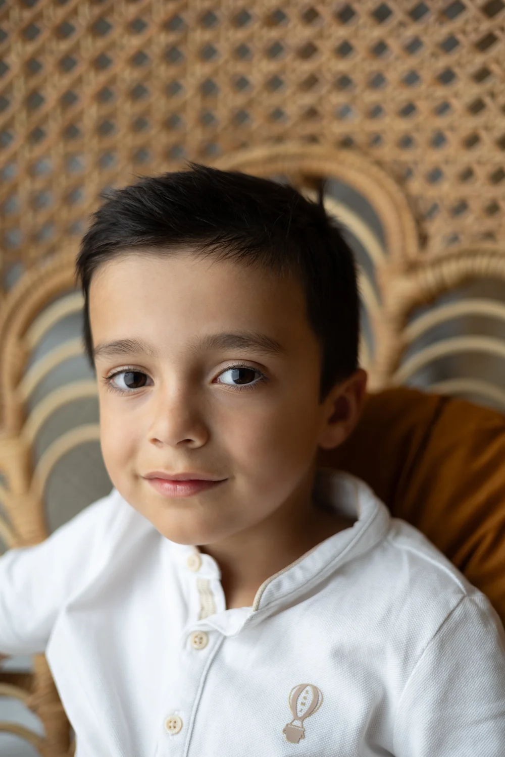 Petit garçon en chemise blanche devant un paravent en rotin.