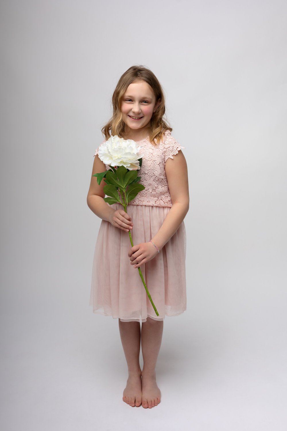 Fillette en robe rose tenant un bouquet, sur fond clair.