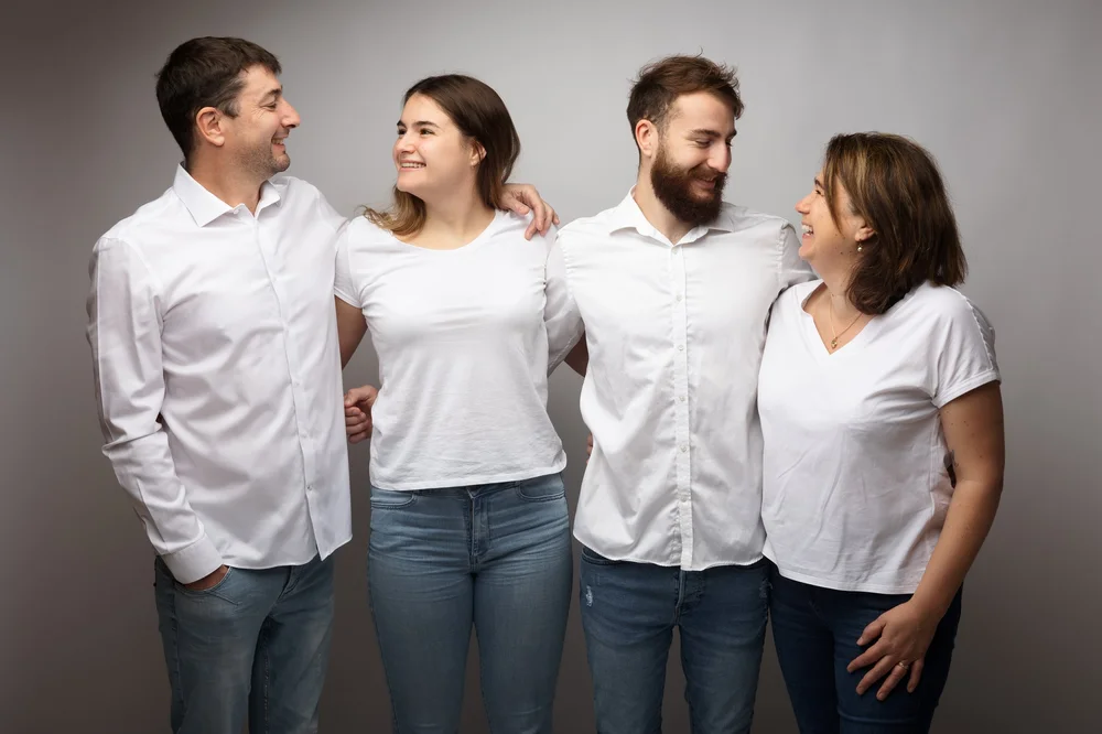 Famille de quatre adultes en chemises blanches, sur fond gris.