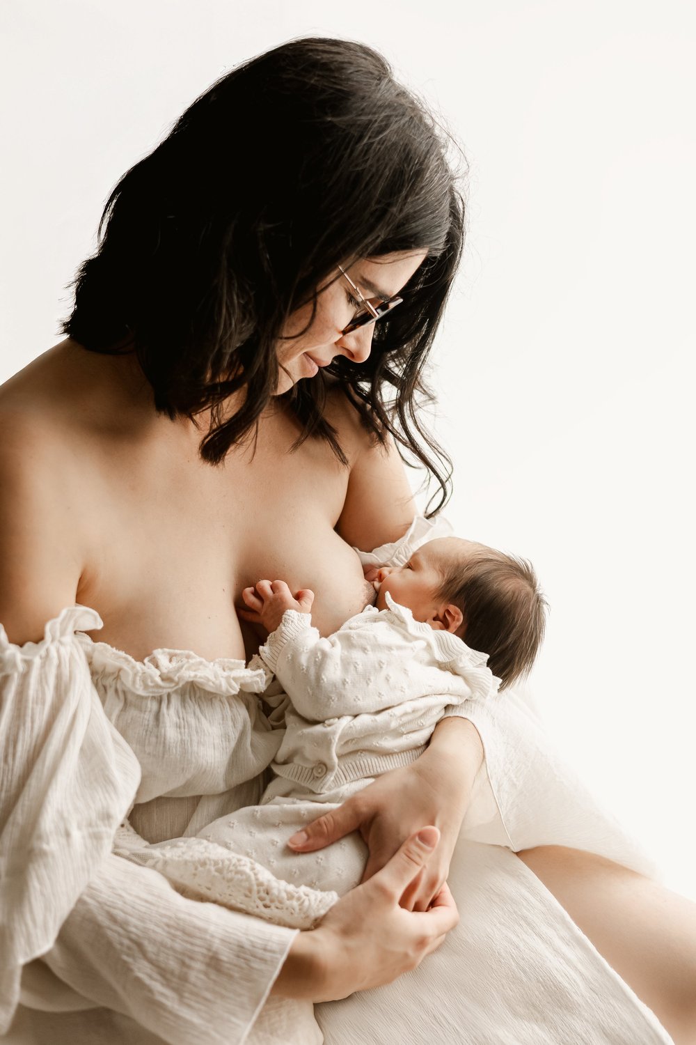 Maman en robe blanche allaitant son nouveau-né, sur fond clair.