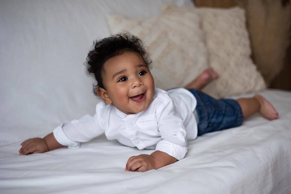 Bébé riant allongé sur le ventre sur un lit blanc.