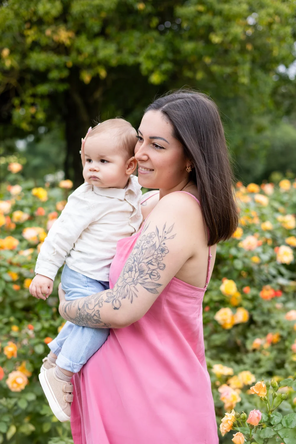 Maman en robe rose portant son bébé contre elle, devant des fleurs orangées.