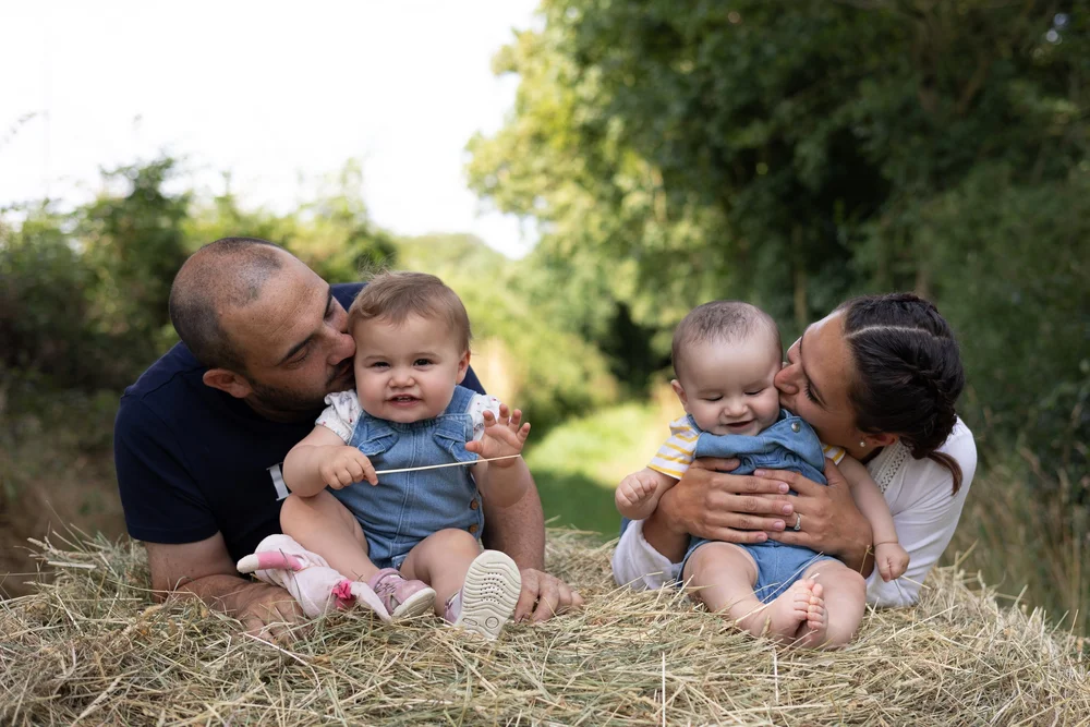 Parents embrassant leurs jumeaux assis dans le foin.