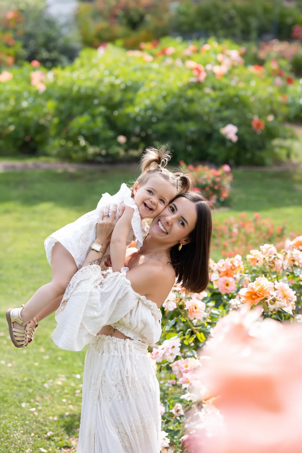 Maman riant en soulevant sa petite fille, au milieu d’un jardin de roses.