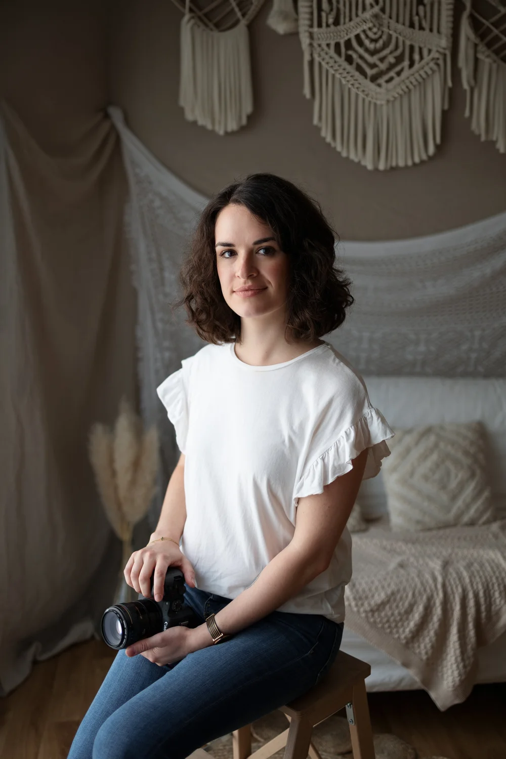 Femme tenant un appareil photo, assise devant un macramé.