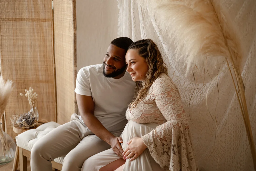 Couple assis en studio, la femme enceinte en robe de dentelle blanche.