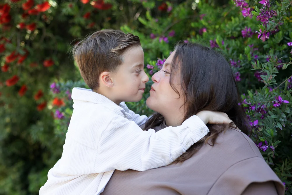 Maman embrassant son fils devant un massif fleuri.