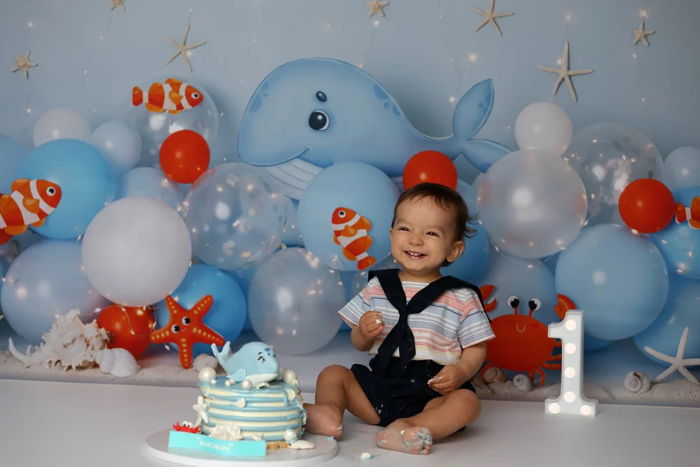 Bébé en tenue de marin avec son gâteau, décor de ballons bleus.