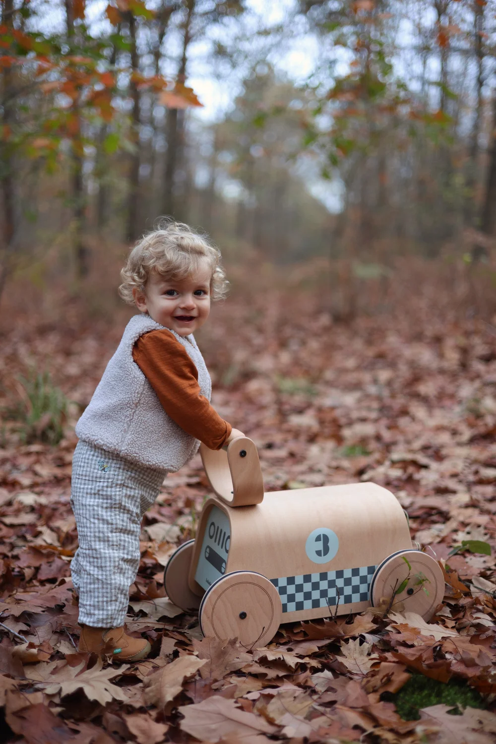 Petit garçon avec un jouet en bois dans les feuilles d’automne.