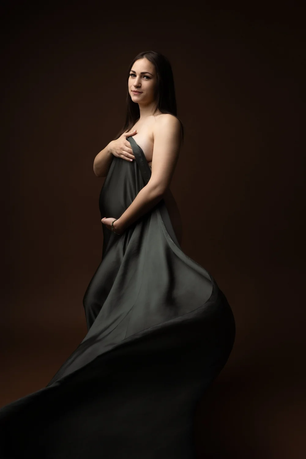 Femme enceinte drapée d’un voile gris anthracite, sur fond brun.