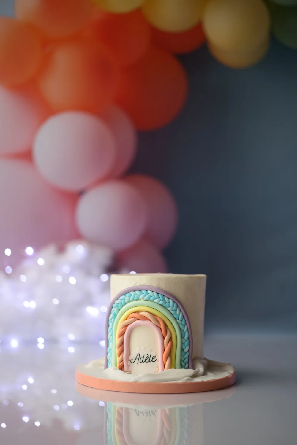 Gâteau arc-en-ciel devant des ballons colorés.