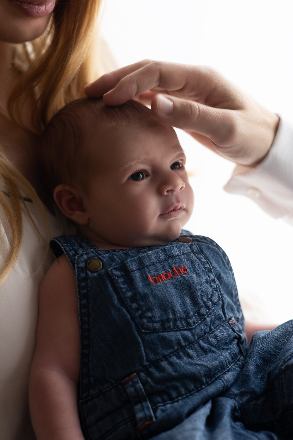 Bébé en salopette en jean, la main de sa maman sur la tête.