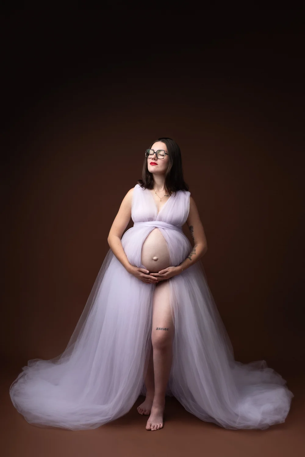 Femme enceinte en robe de tulle lilas, en studio sur fond brun.