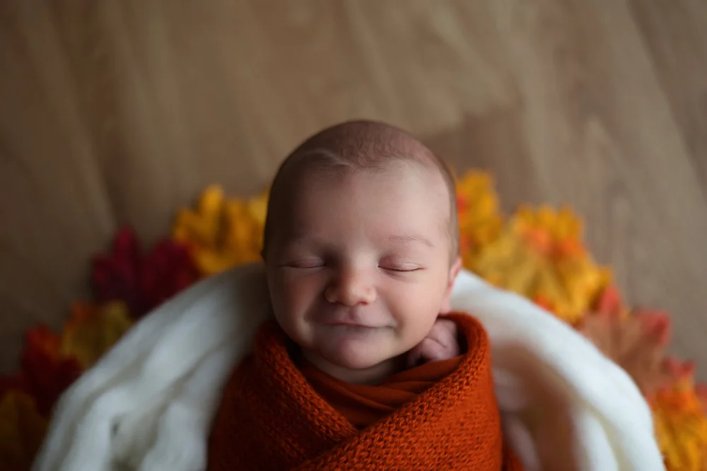Nouveau-né souriant emmailloté de rouille, feuilles d’automne.