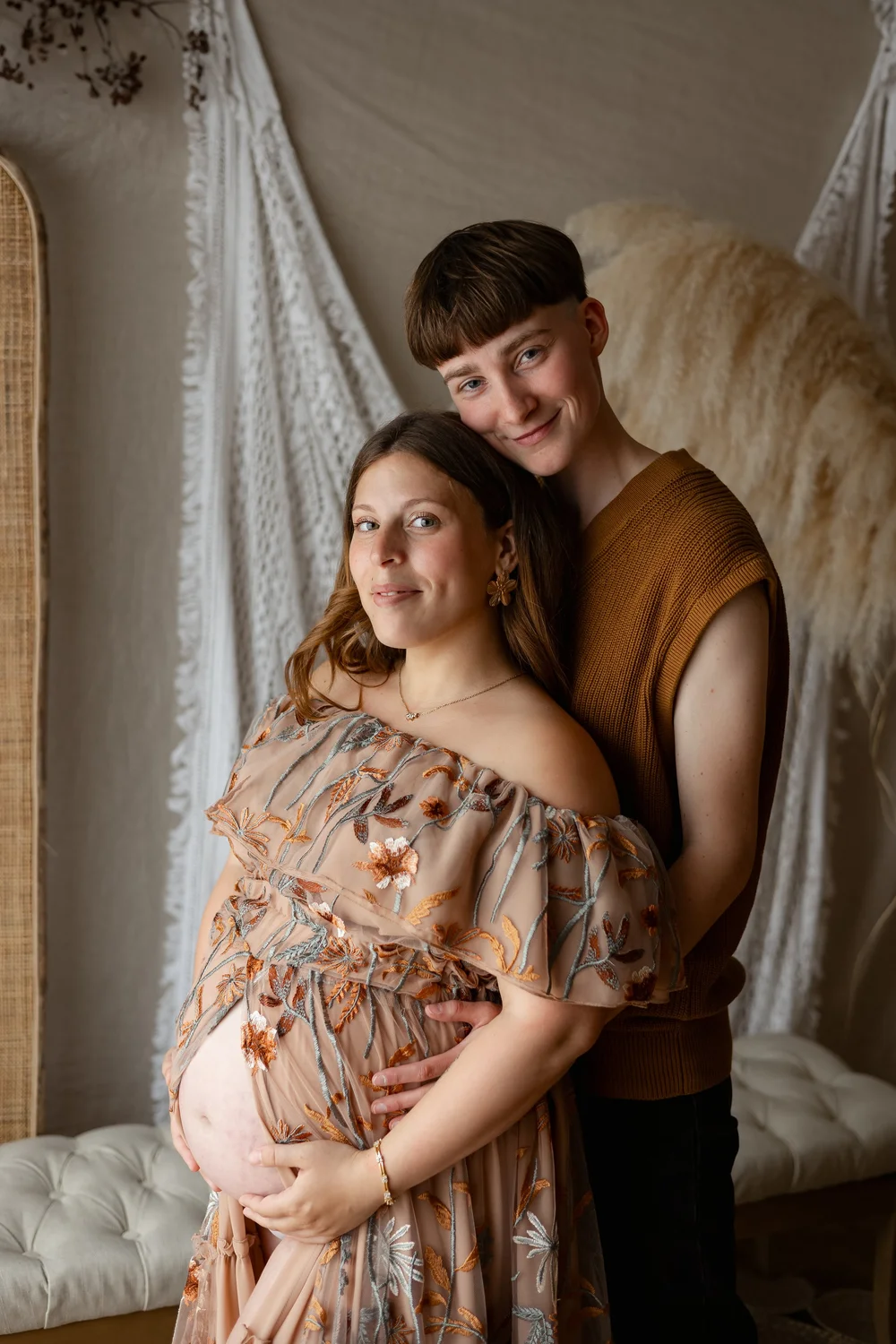 Couple assis en studio devant un paravent, la femme enceinte en robe fleurie.