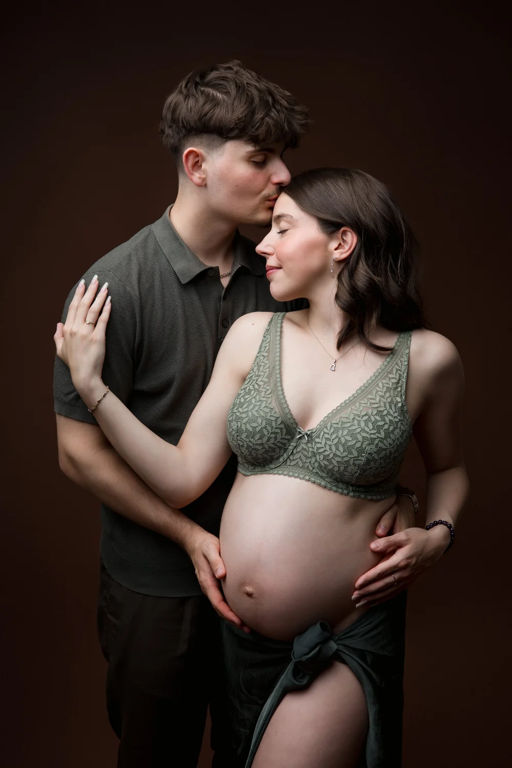 Couple en studio, la femme enceinte en brassière verte, mains sur le ventre.