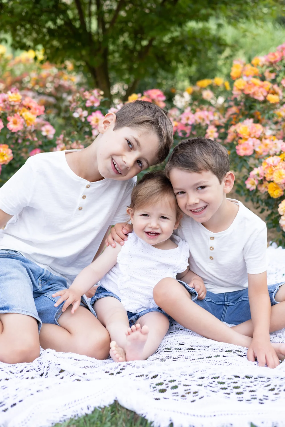Trois frères en t-shirt blanc assis devant des rosiers.