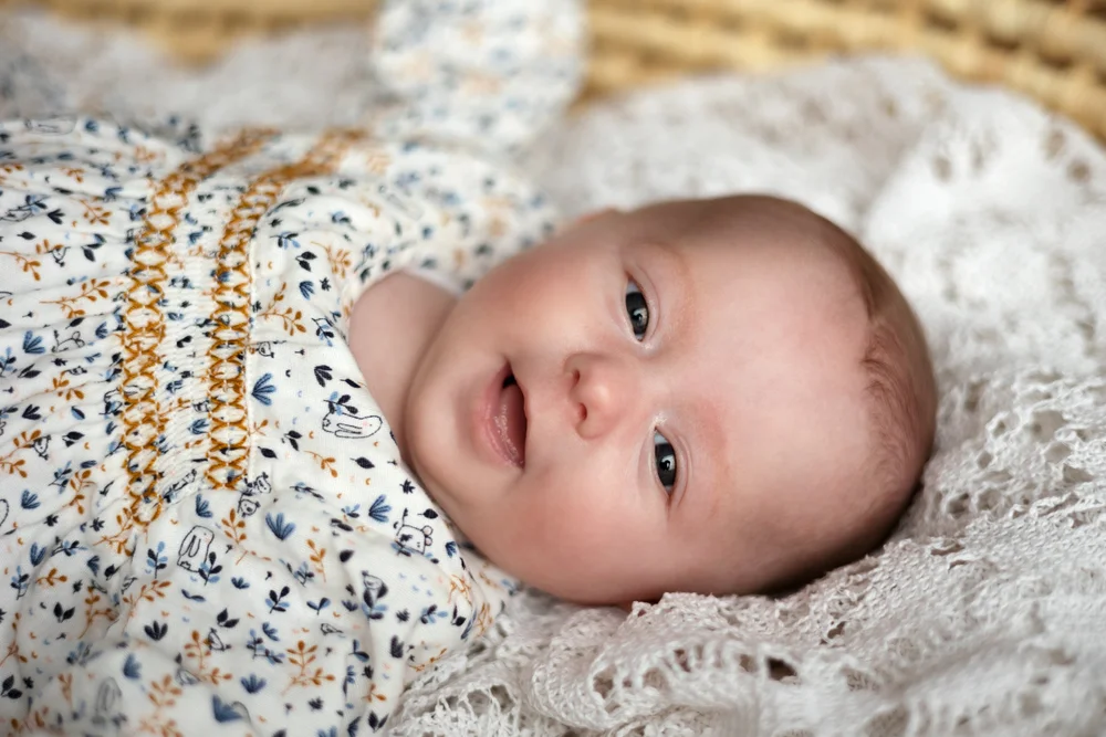 Bébé en tenue fleurie allongée sur une couverture, vue de dessus.