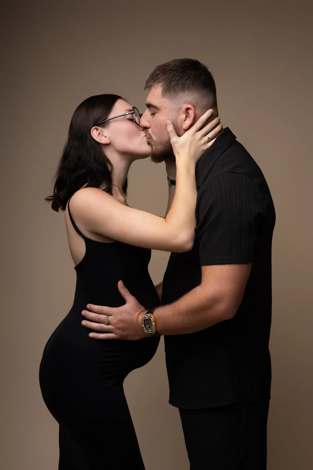 Couple s’embrassant en studio, la femme enceinte en robe noire.