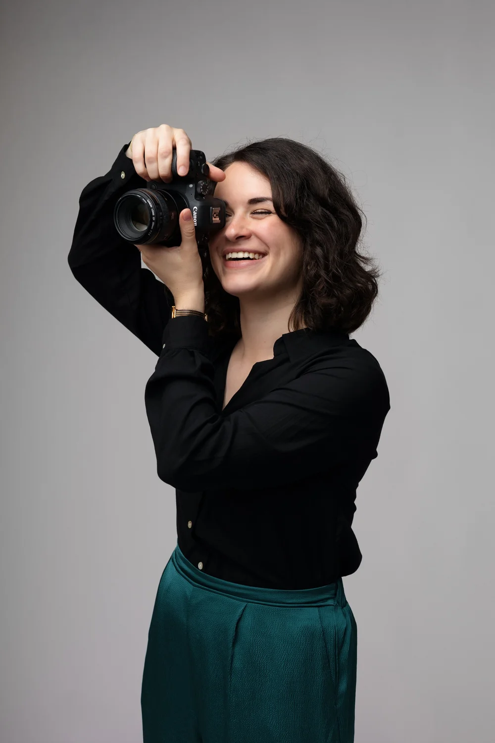 Femme souriante tenant un appareil photo, sur fond gris.