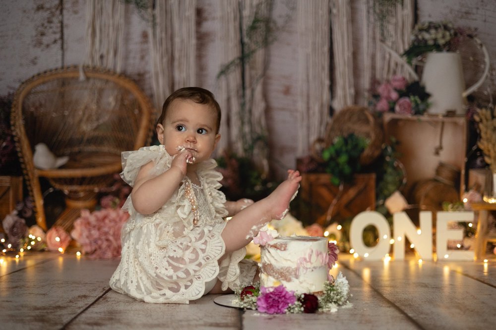 Bébé en robe de dentelle goûtant son gâteau devant les lettres « ONE ».