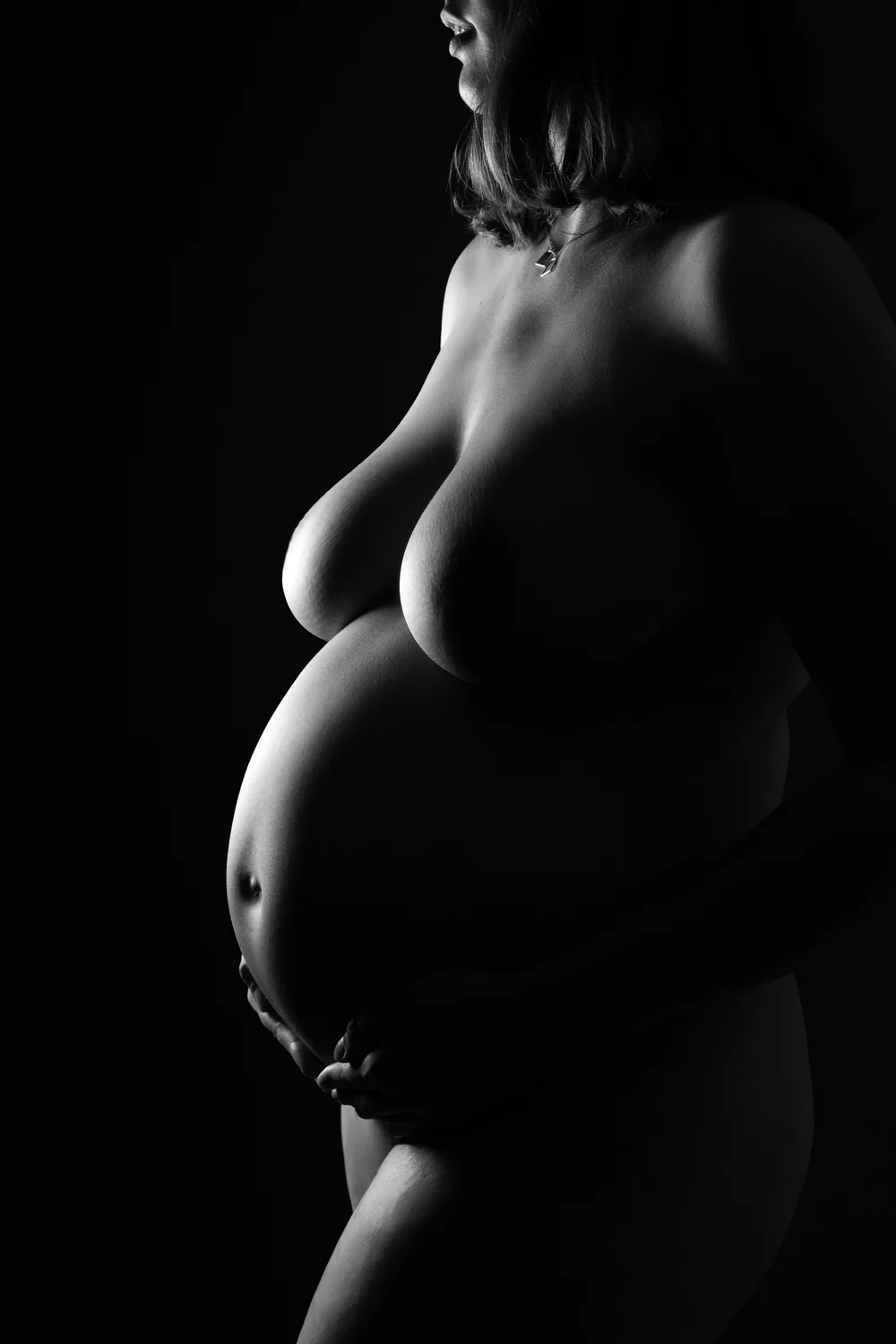 Femme enceinte en clair-obscur, sur fond noir.