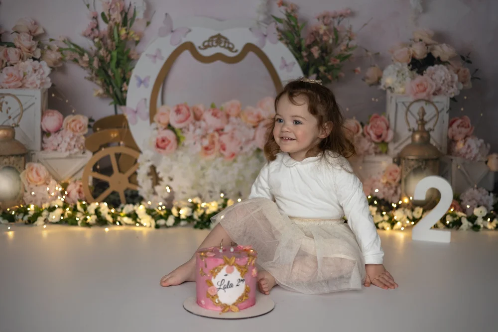 Petite fille devant un décor fleuri avec un chiffre 2 et son gâteau.