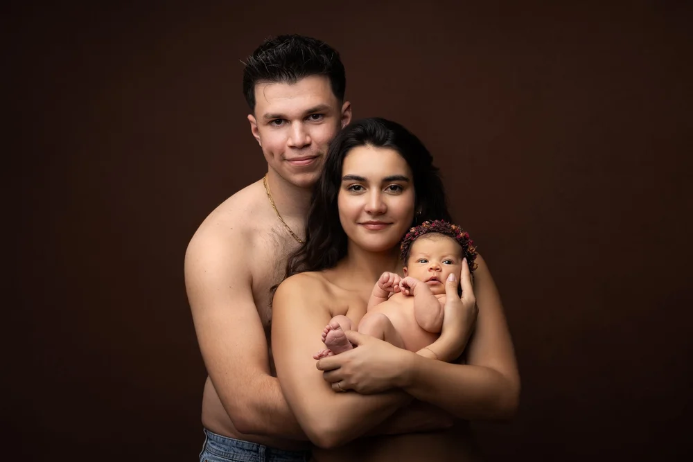 Parents en studio sur fond brun, le nouveau-né contre eux.