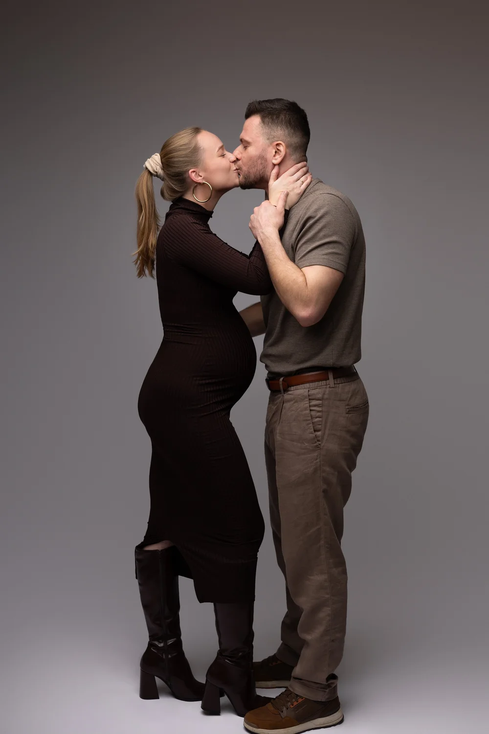 Couple s’embrassant en studio, la femme enceinte en robe noire.