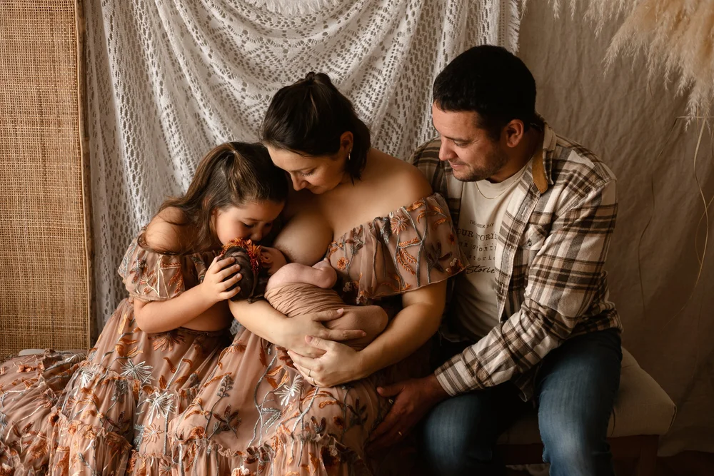 Famille assise dans le studio, la maman allaitant le nouveau-né entre sa fille et le papa.