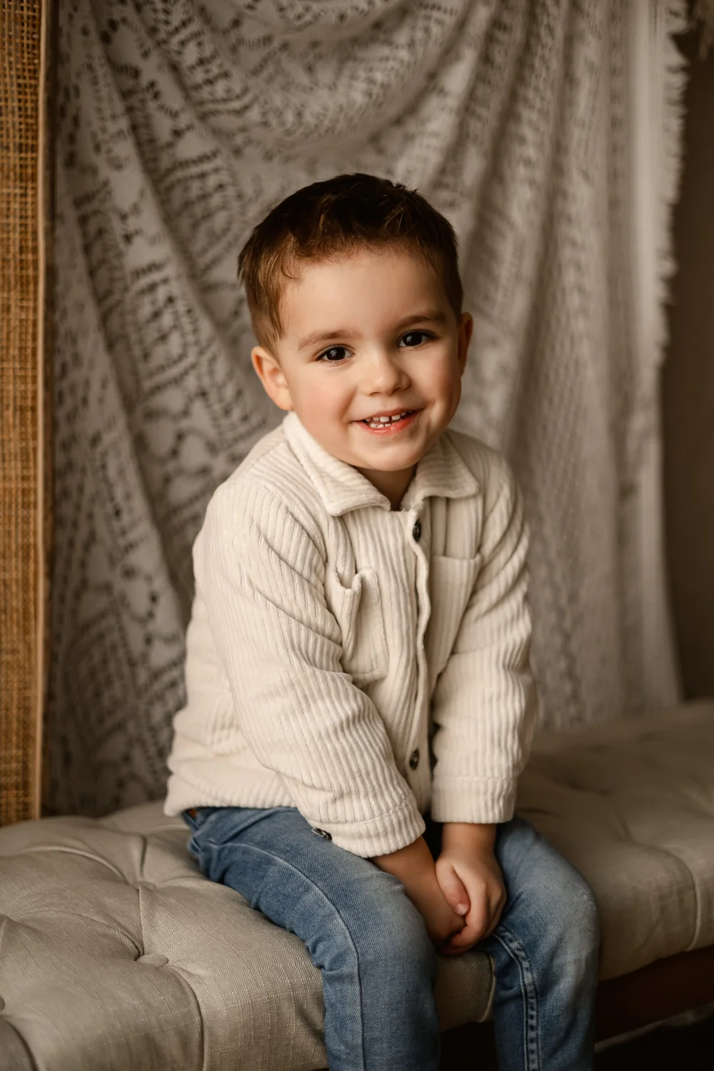 Petit garçon souriant en pull beige, assis sur une banquette capitonnée.
