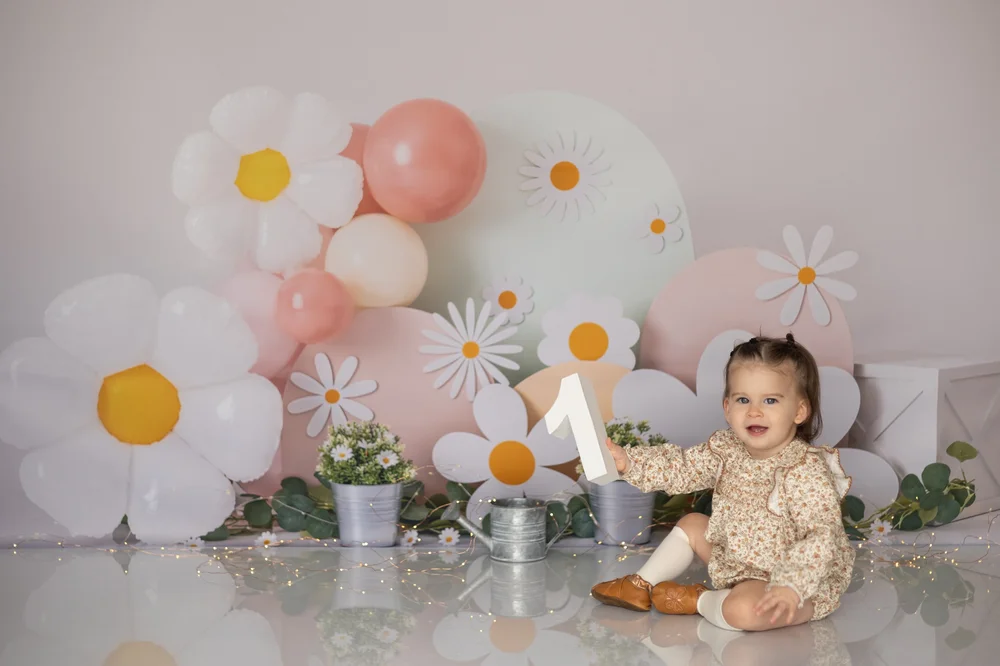 Bébé assis devant un décor de ballons et de marguerites.