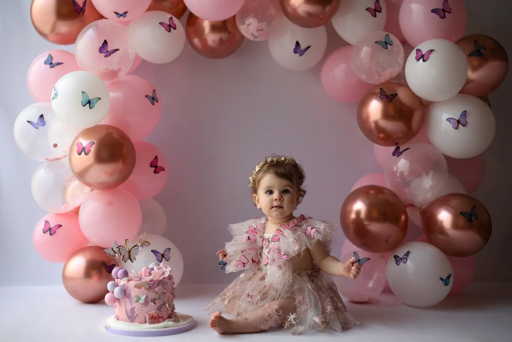 Petite fille devant une arche de ballons roses et cuivrés avec son gâteau.