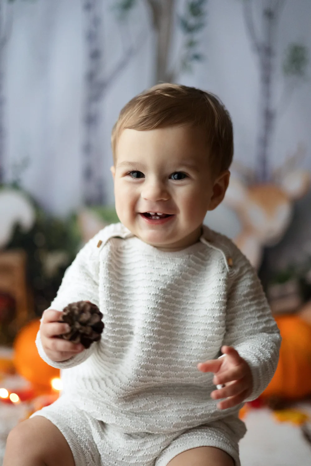 Bébé souriant en pull blanc, décor d’automne.