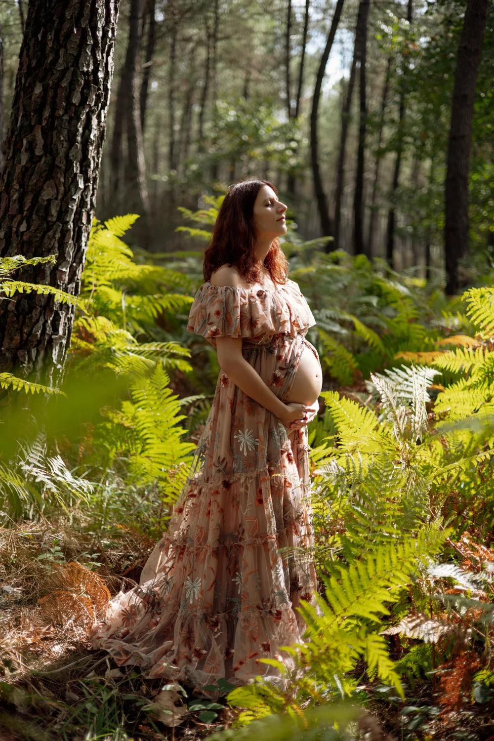 Femme enceinte en robe fleurie au milieu des fougères, en forêt.