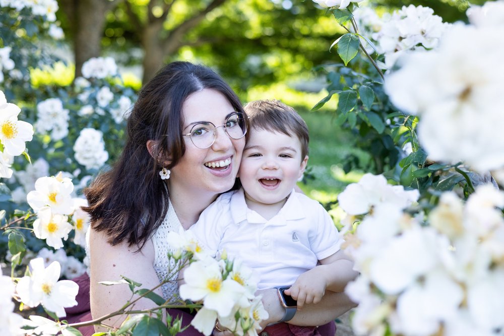 Maman et son petit garçon rieurs au milieu de roses blanches.