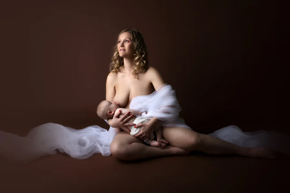 Maman drapée de tulle allaitant son bébé, sur fond brun.