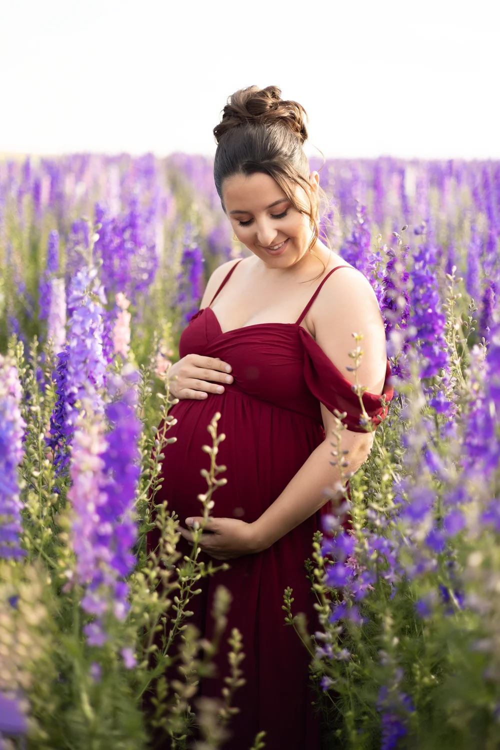 Femme enceinte en robe bordeaux dans un champ de fleurs violettes.