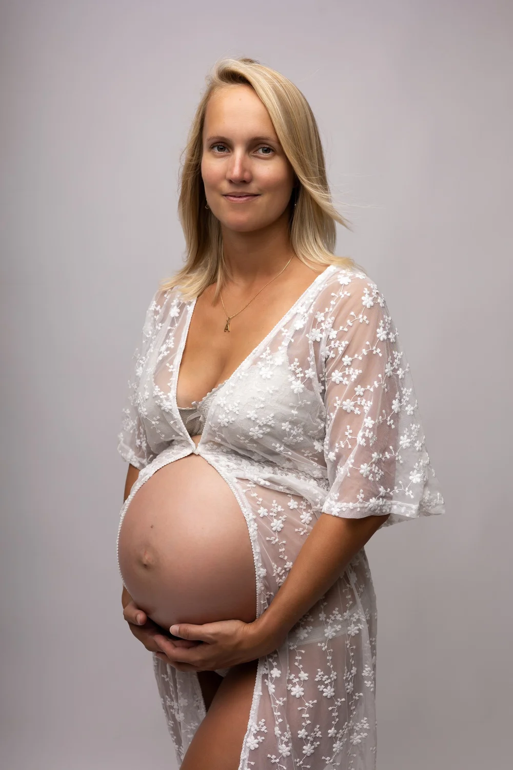 Femme enceinte en kimono de dentelle blanche, sur fond clair.