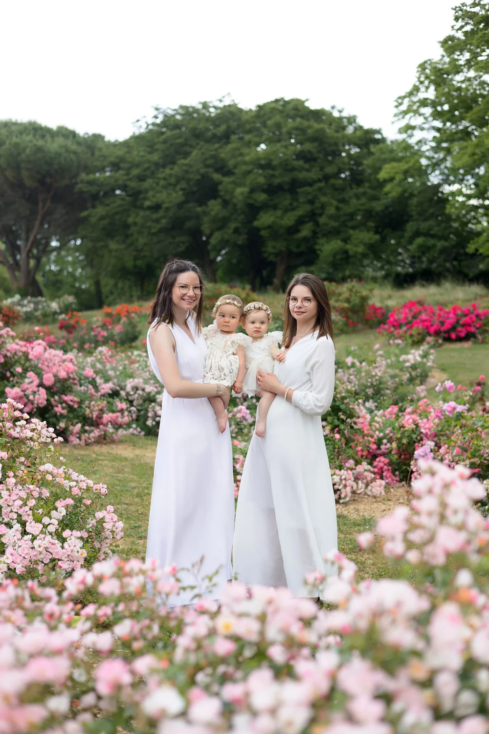 Deux mamans en robe blanche avec leur bébé dans une roseraie.