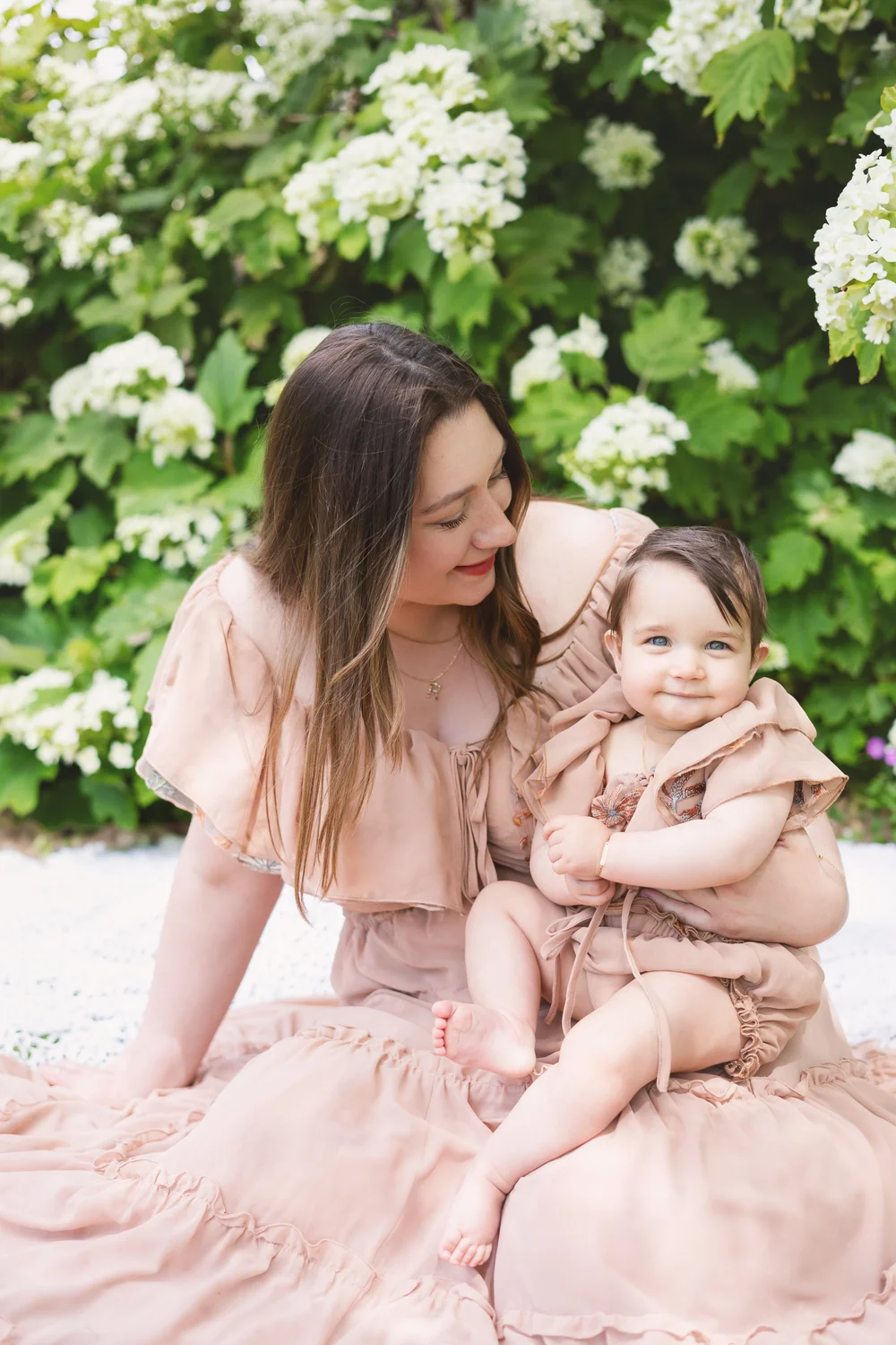 Maman et sa fille en robes roses assises devant des hortensias blancs.
