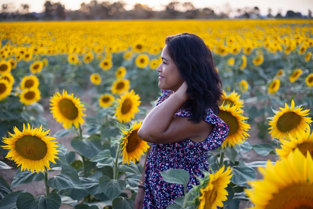 Femme en robe fleurie dans un champ de tournesols.