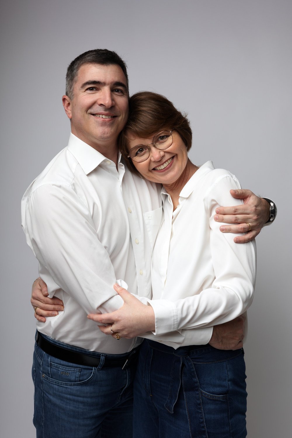Couple enlacé en chemises blanches, sur fond gris.