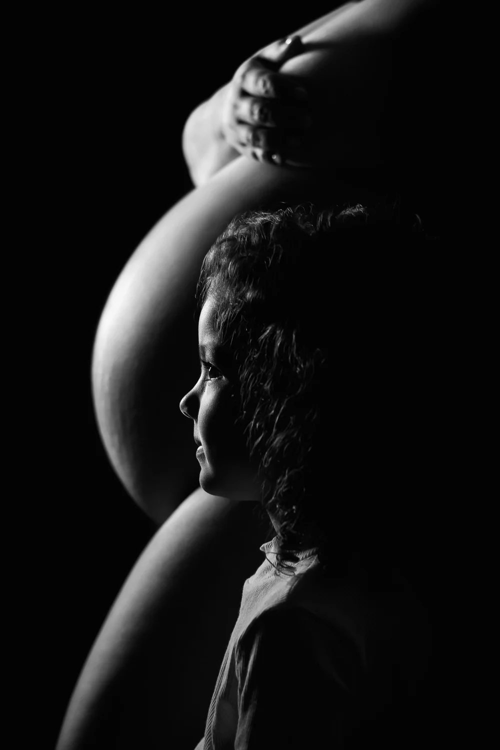 Portrait en noir et blanc : un enfant de profil devant le ventre rond de sa mère.