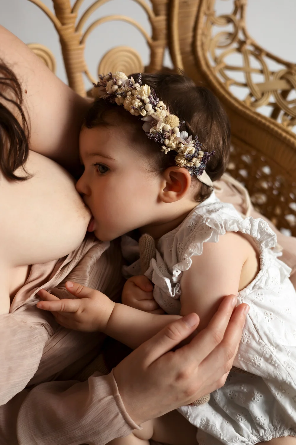 Bébé couronné de fleurs au sein de sa maman, dans un fauteuil en rotin.