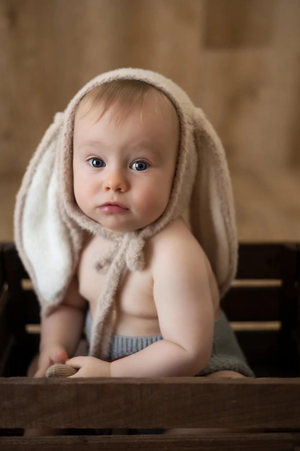 Bébé en bonnet de lapin assis dans une caisse en bois.