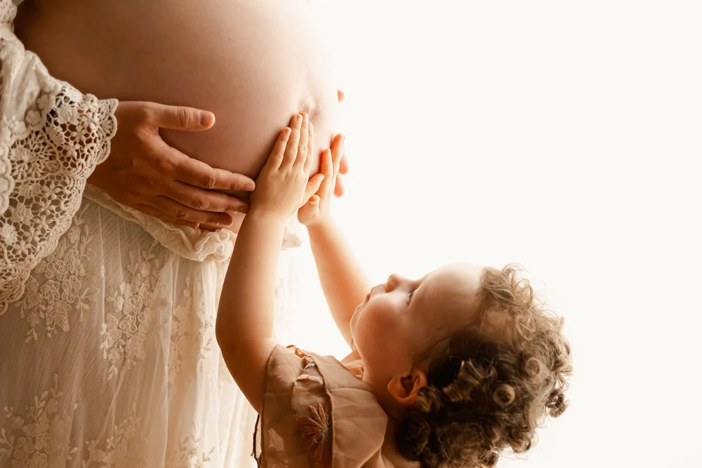 Petit enfant posant les mains sur le ventre de sa maman, en contre-jour.