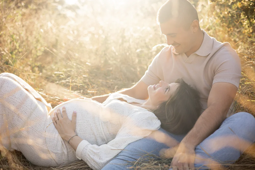 Femme enceinte allongée contre son conjoint dans les hautes herbes, au soleil couchant.