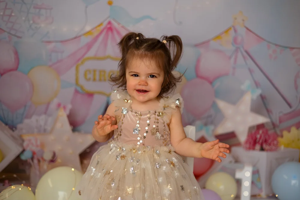 Petite fille en robe beige devant un décor de cirque pastel.