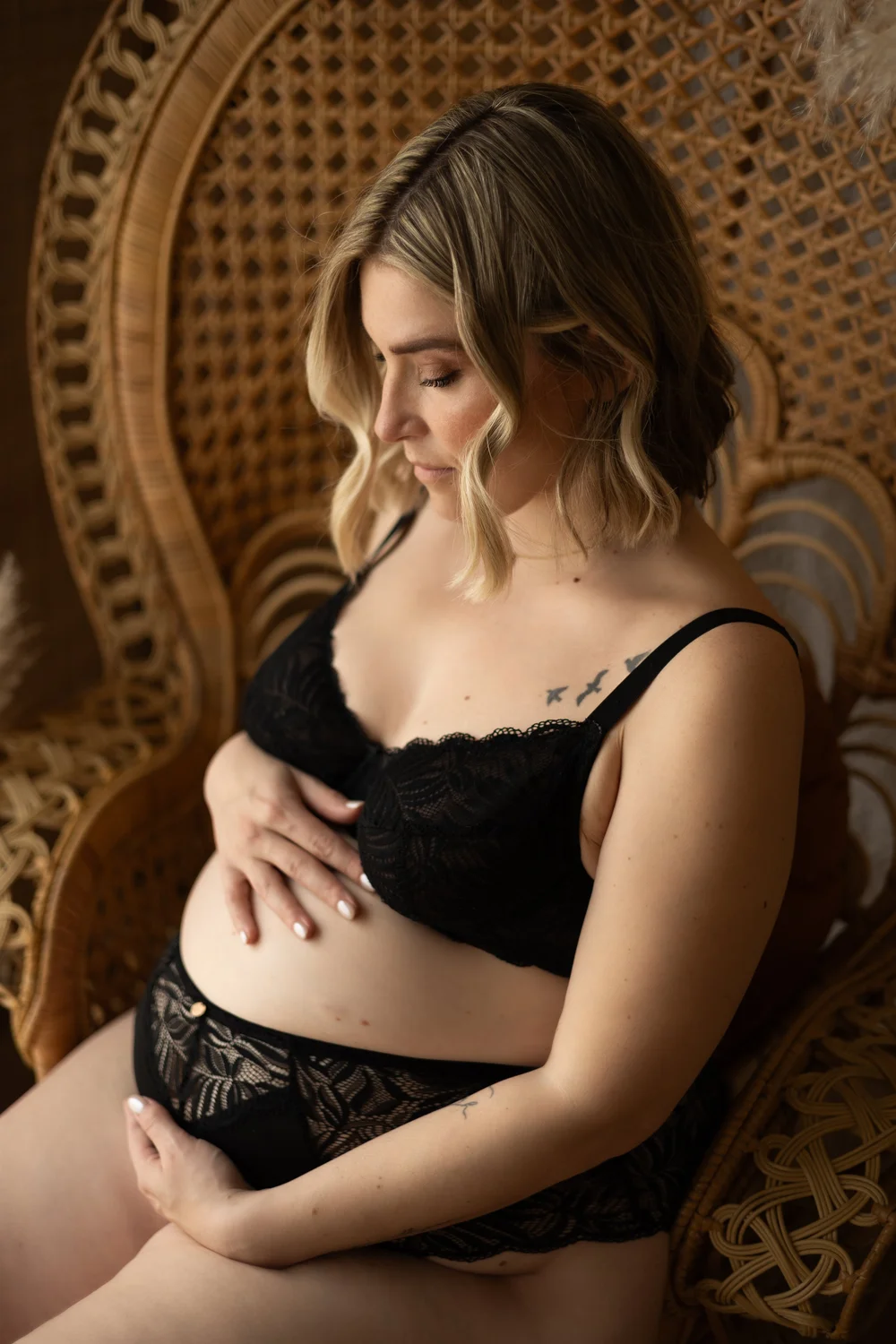 Femme enceinte en lingerie noire dans un fauteuil en rotin.